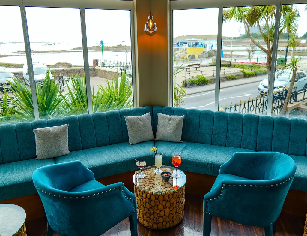 Stylish bar seating area with turquoise sofas and cocktails beside large windows overlooking the seafront