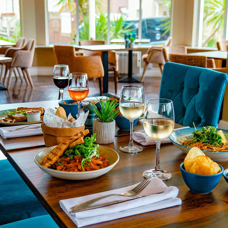 Table set with pasta dishes, bread, crisps and glasses of wine inside Coast Bistro