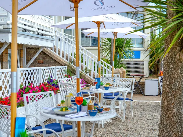 Outdoor dining terrace at Ommaroo Hotel with white umbrellas, tables set with food and drinks, and bright flower planters