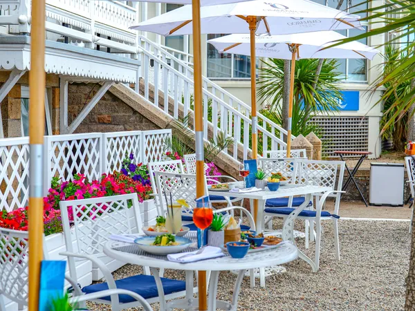 Outdoor dining terrace at Ommaroo Hotel with white umbrellas, tables set with food and drinks, and bright flower planters