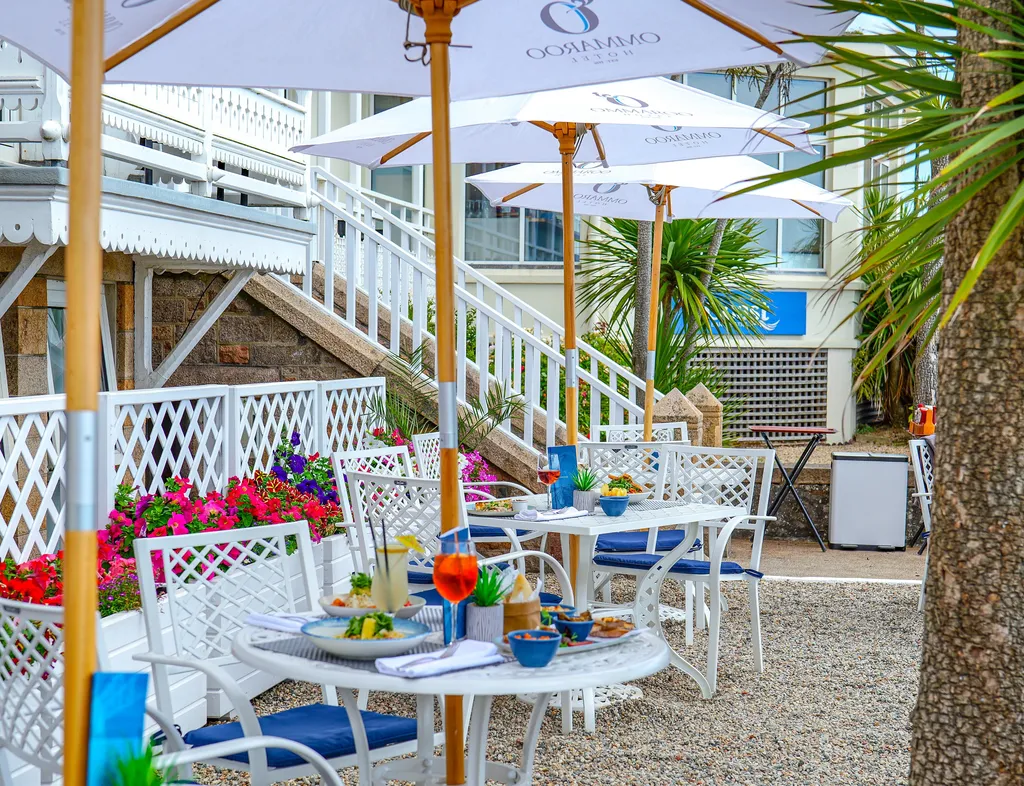 Outdoor dining terrace at Ommaroo Hotel with white umbrellas, tables set with food and drinks, and bright flower planters