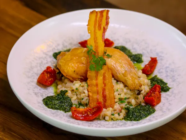 Roast chicken served on creamy risotto with crispy bacon, pesto and roasted cherry tomatoes