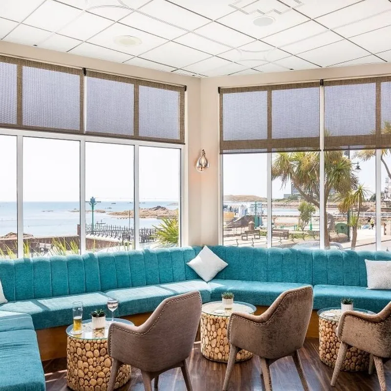 Stylish coastal bar lounge with turquoise seating, armchairs and sea views through large windows