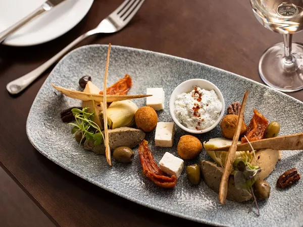 Mediterranean-style sharing platter with feta, olives, sun-dried tomatoes, artichokes and a herb dip on a grey serving plate