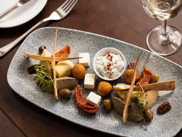 Mediterranean-style sharing platter with feta, olives, sun-dried tomatoes, artichokes and a herb dip on a grey serving plate