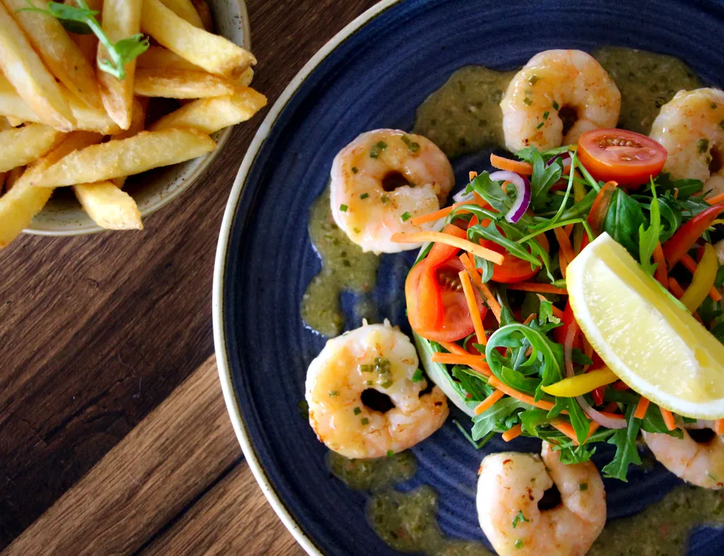 Prawns arranged around a fresh mixed salad with a lemon wedge, served with chips on a wooden table.