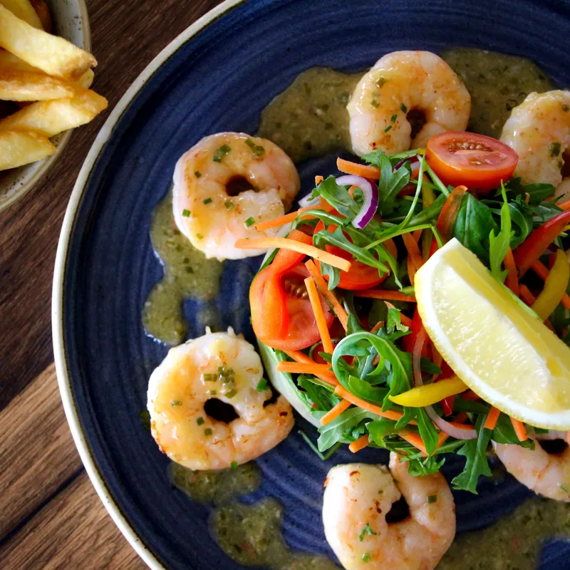 Prawns arranged around a fresh mixed salad with a lemon wedge, served with chips on a wooden table.