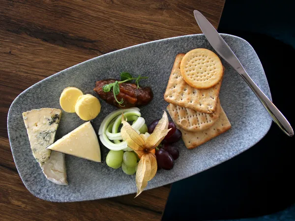 Cheese board with assorted cheeses, crackers, grapes, butter and chutney on a grey platter
