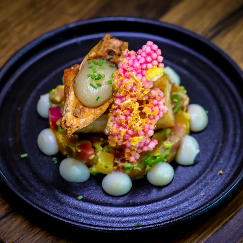 Artfully presented gourmet dish on a black plate with colourful garnishes and sauce dots at Palmers Restaurant