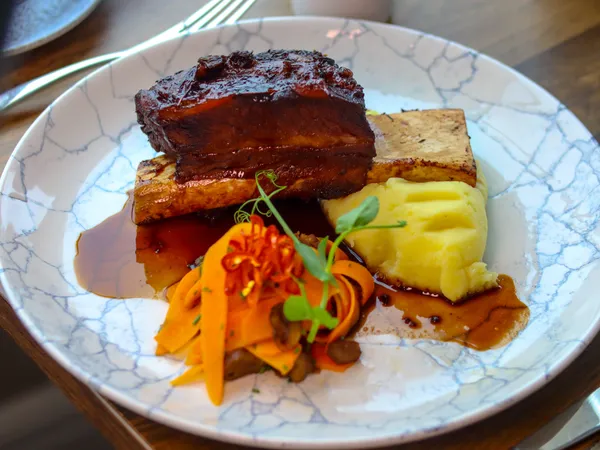 Braised pork belly served with creamy mashed potato, glazed carrots and rich gravy on a marble-patterned plate