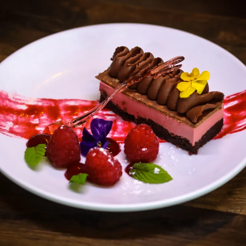 Chocolate and raspberry dessert slice served on a white plate with fresh raspberries, berry sauce, mint leaves and edible flowers at Palmers Restaurant