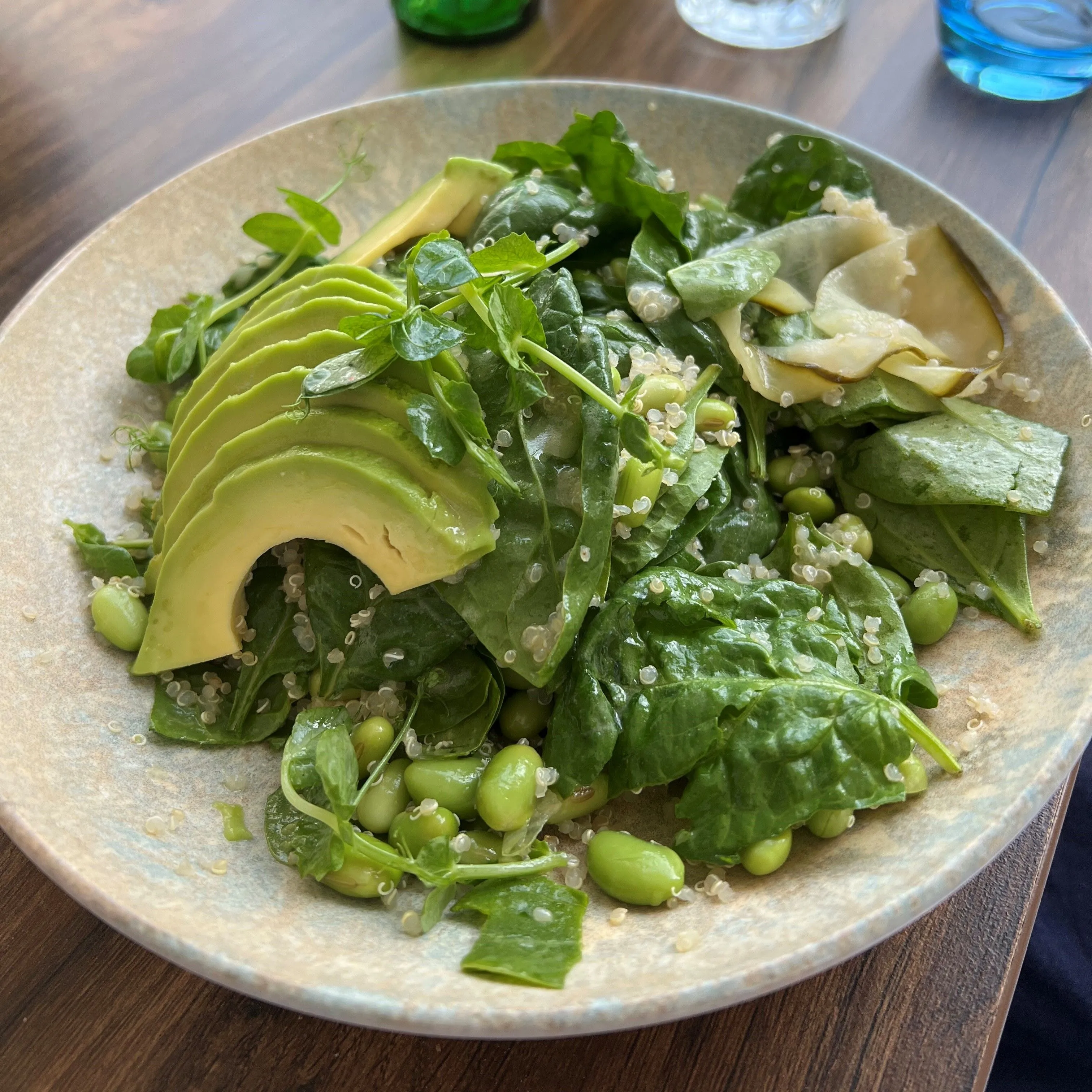 Fresh green salad with sliced avocado, spinach, edamame beans and quinoa on a restaurant table