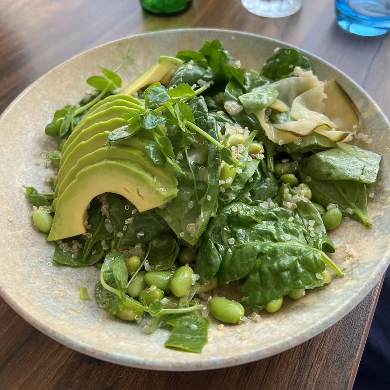 Fresh green salad with sliced avocado, spinach, edamame beans and quinoa on a restaurant table