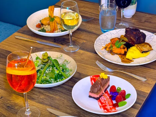 A restaurant table set with several plated dishes, including grilled pork chop, braised meat, salad, dessert and drinks.