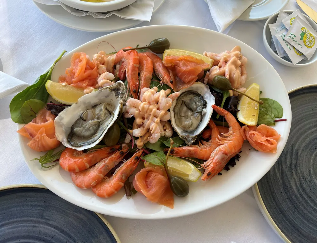 Seafood platter with prawns, oysters, smoked salmon, lemon wedges and mixed leaves on a white oval plate at Palmers Restaurant