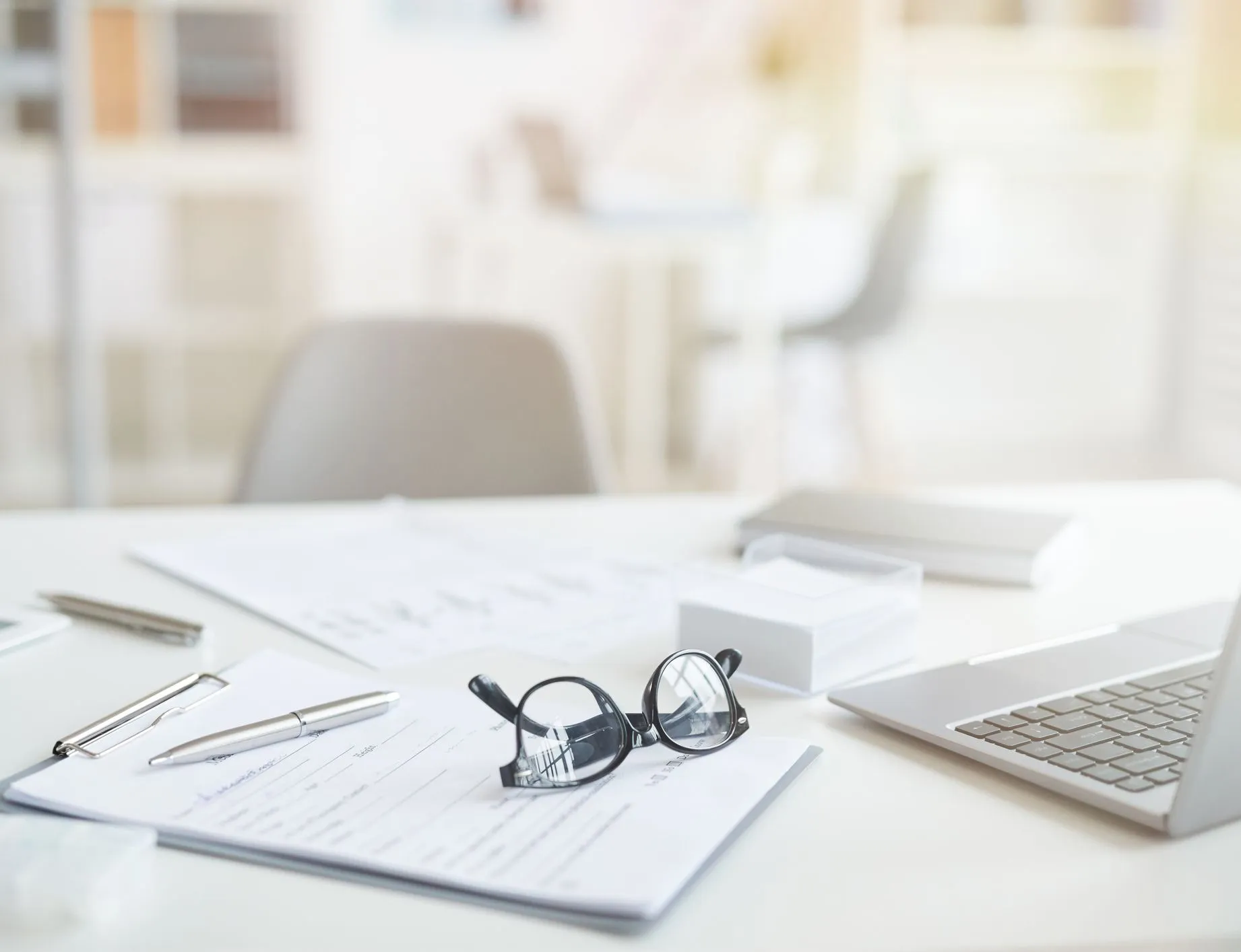 Bright office desk with paperwork, spectacles, pen, tablet and laptop