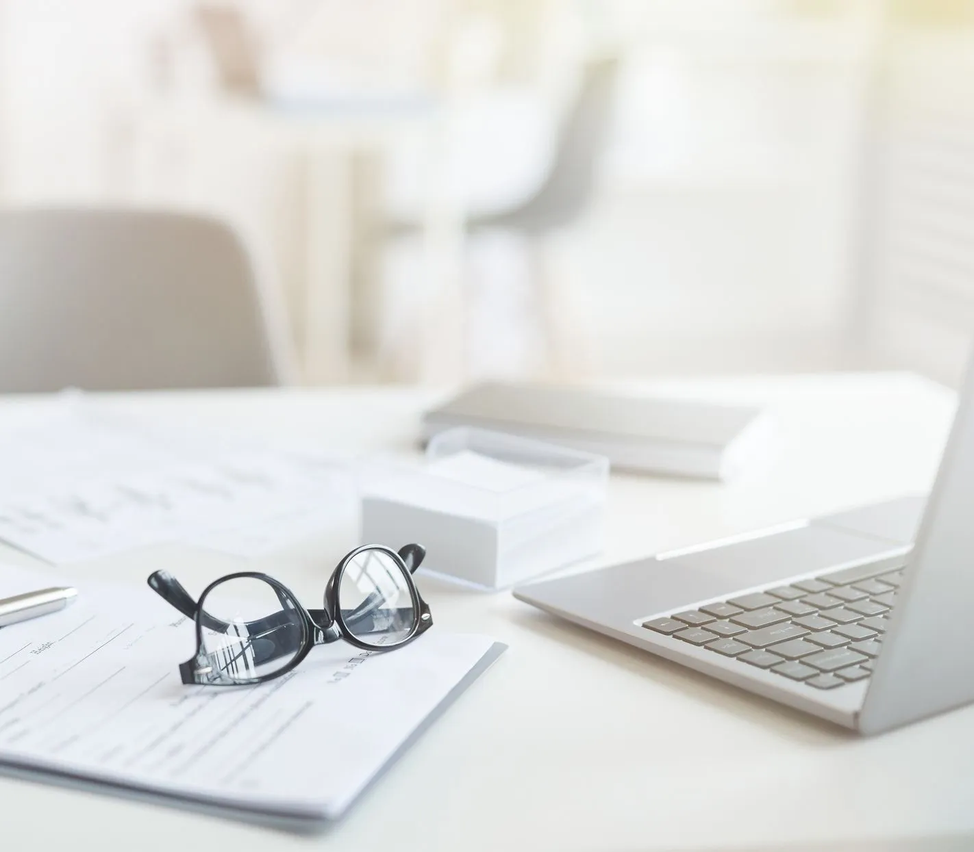 Bright office desk with paperwork, spectacles, pen, tablet and laptop