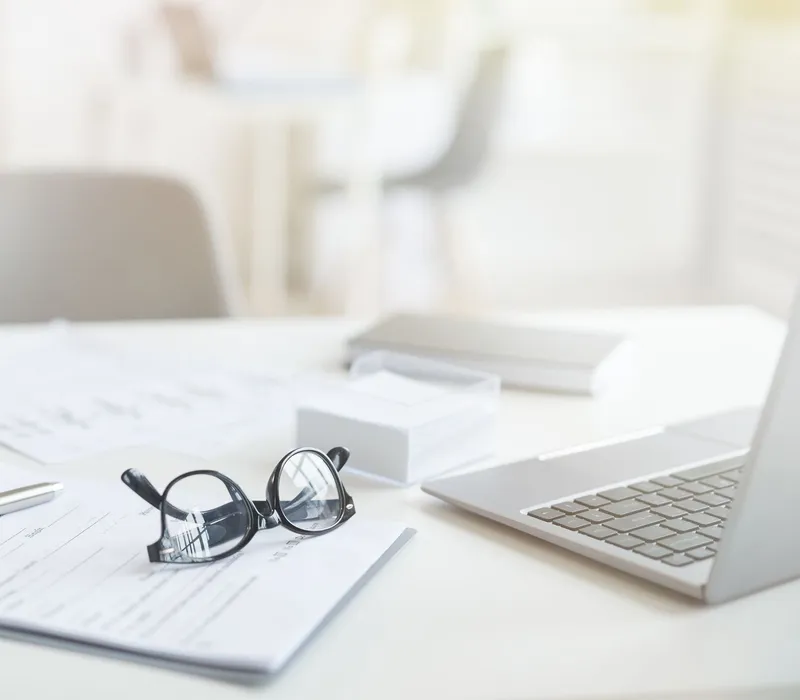 Bright office desk with paperwork, spectacles, pen, tablet and laptop