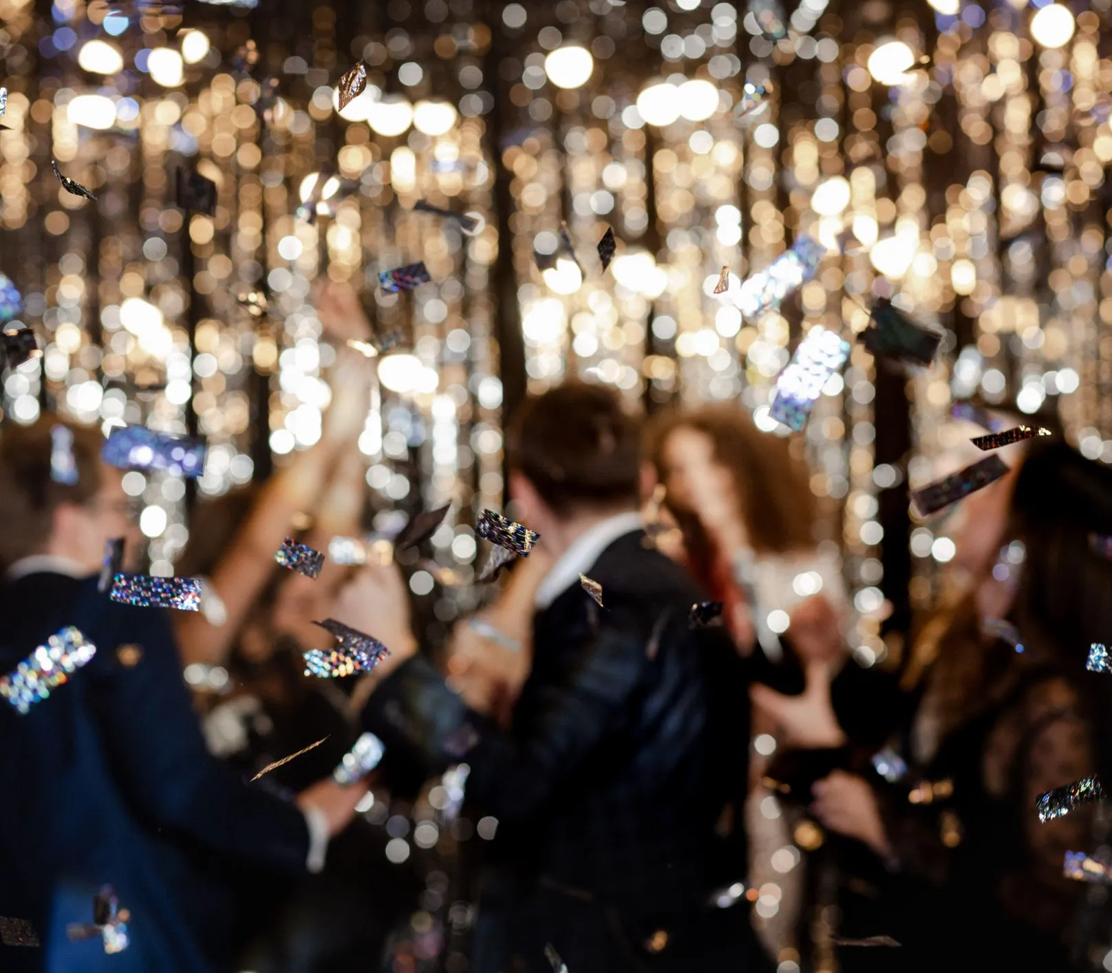 Blurred party guests celebrating with falling confetti against sparkling lights