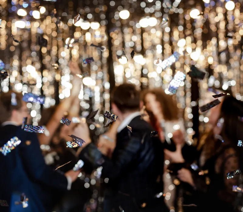 Blurred party guests celebrating with falling confetti against sparkling lights
