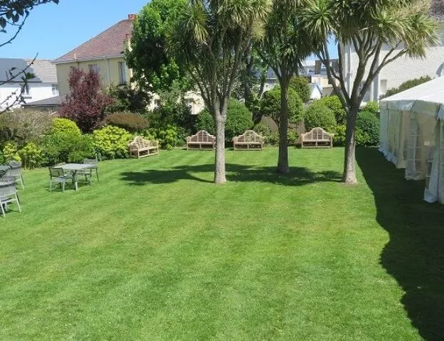 Landscaped garden with a neatly mown lawn, mature trees, benches and outdoor seating beside a marquee
