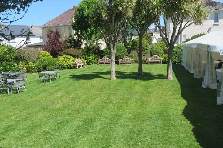 Landscaped garden with a neatly mown lawn, mature trees, benches and outdoor seating beside a marquee