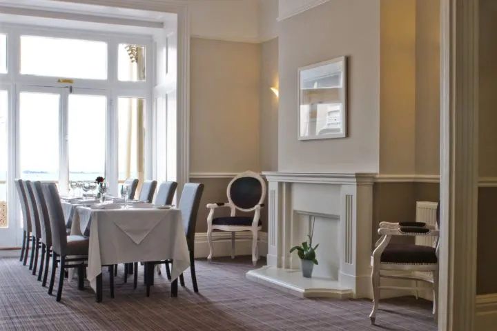 Elegant hotel salon dining room with white-clothed tables, upholstered chairs and large windows