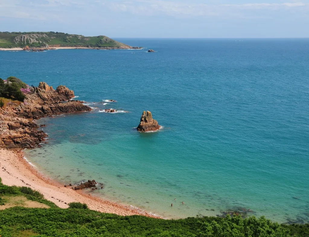 View over Beauport bay with turquoise sea, rocky cliffs and a small sandy beach.