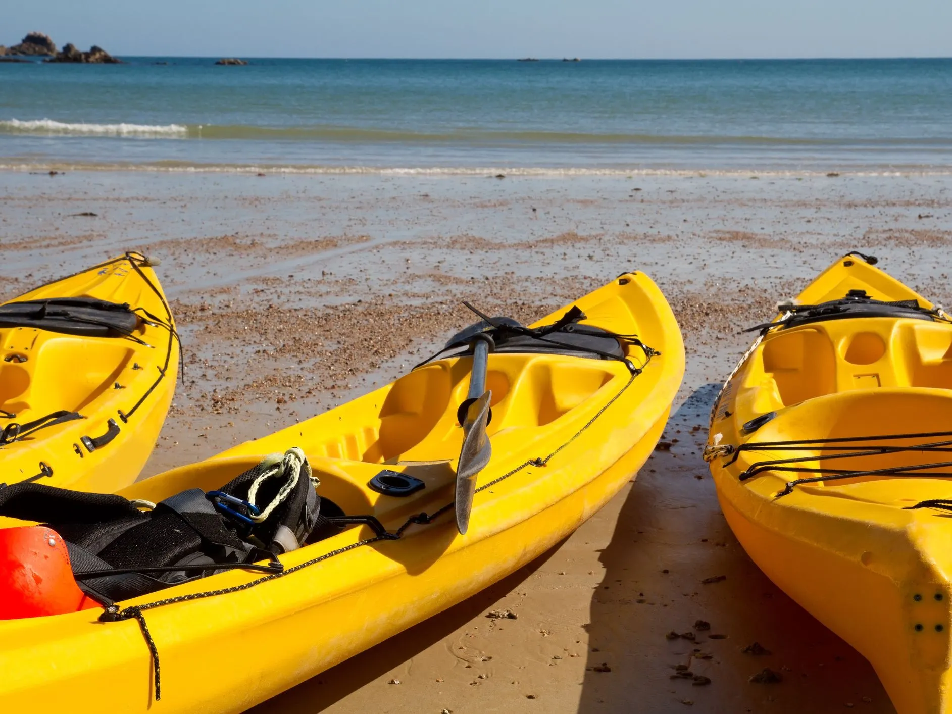 Three yellow kayaks resting on a sandy beach beside calm blue sea.