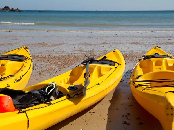 Three yellow kayaks resting on a sandy beach beside calm blue sea.