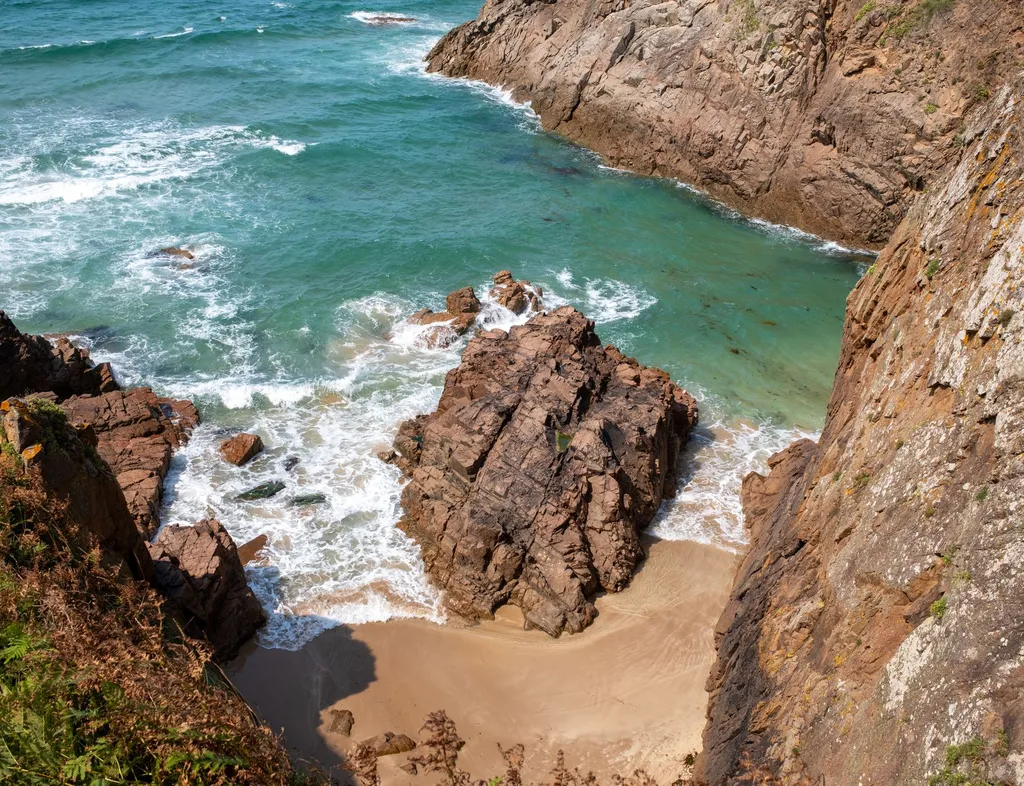 Rocky coastal cove with turquoise sea, foaming waves and a small sandy beach below steep cliffs
