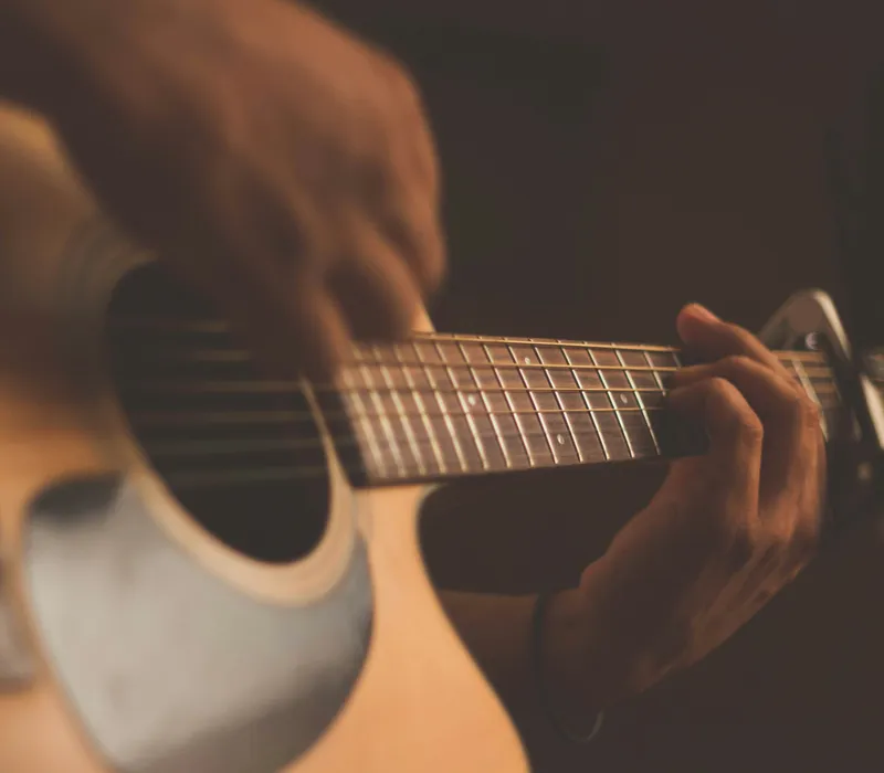 Close-up of hands playing an acoustic guitar in warm, low light