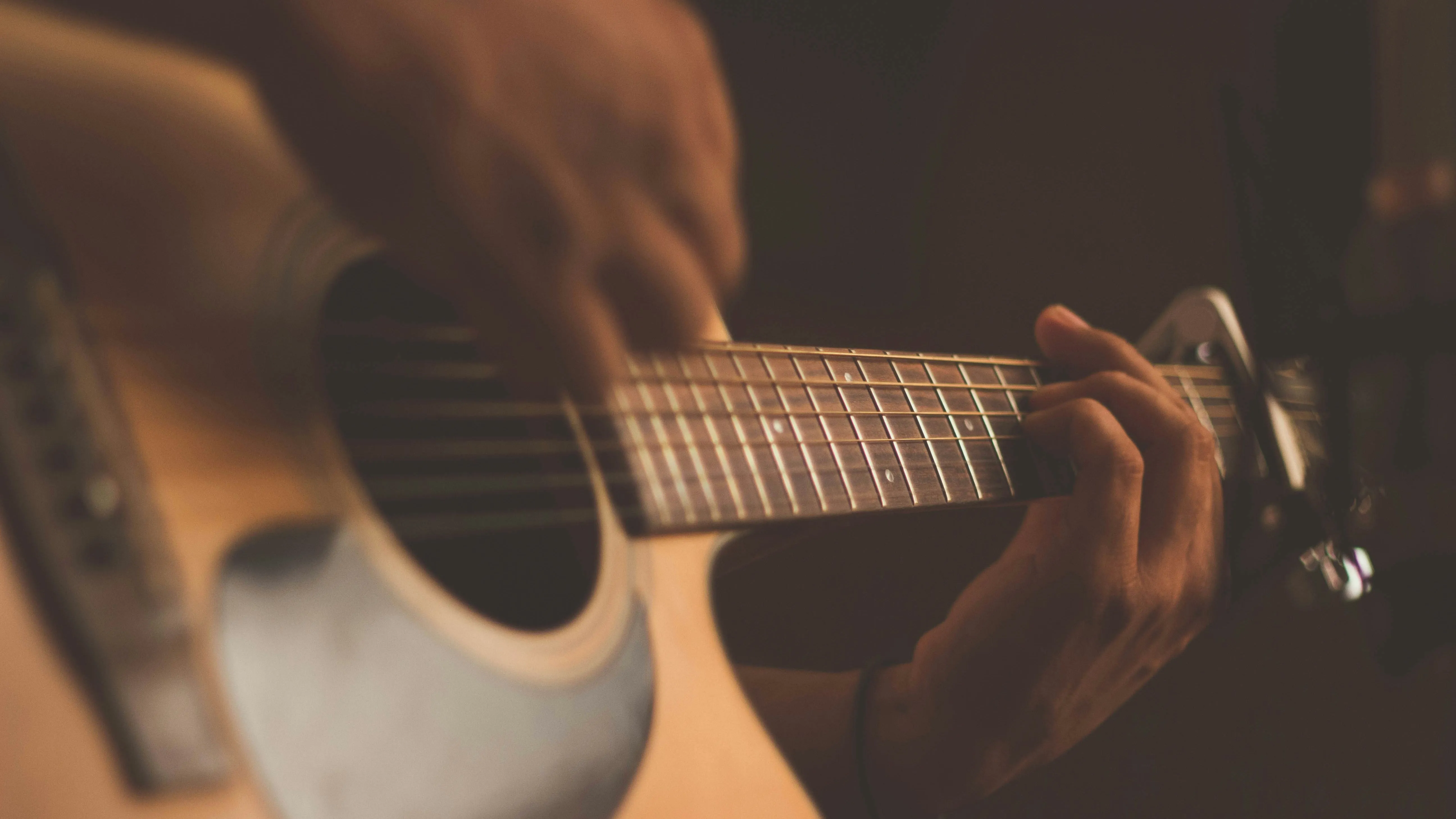 Close-up of hands playing an acoustic guitar in warm, low light