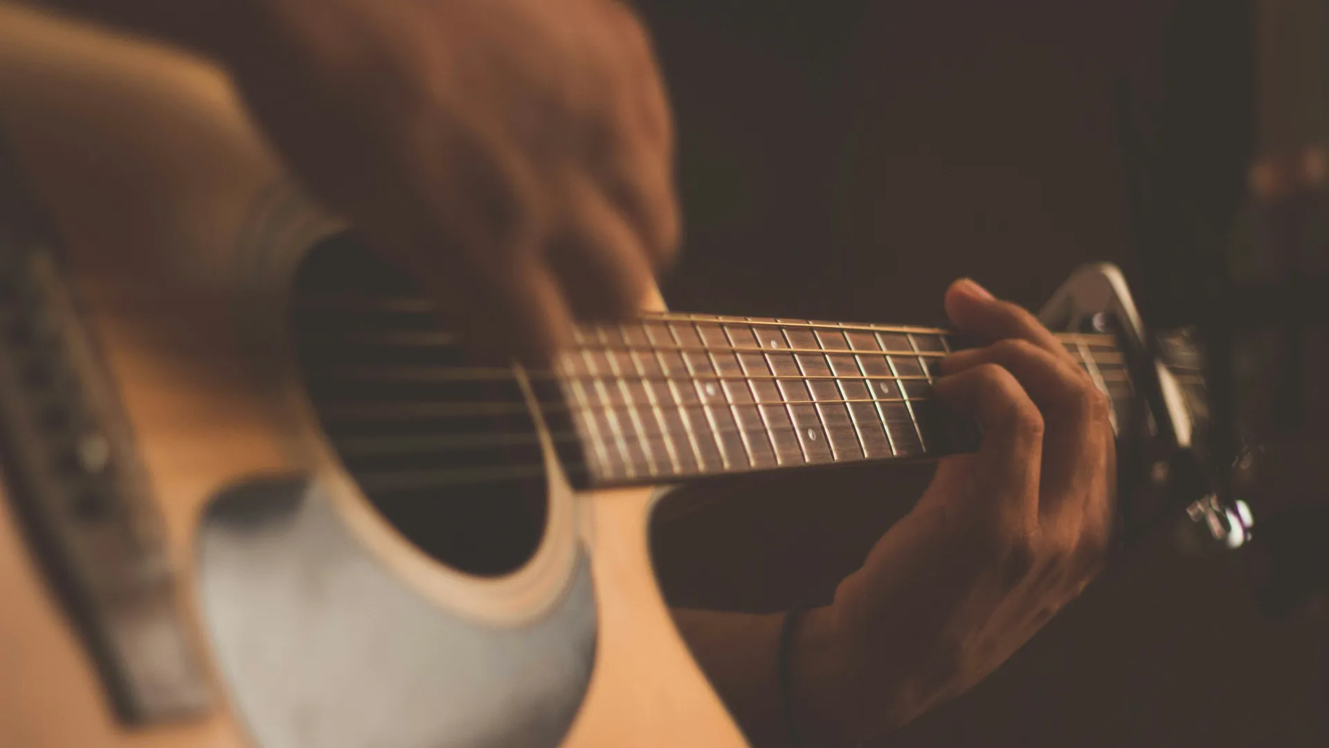 Close-up of hands playing an acoustic guitar in warm, low light