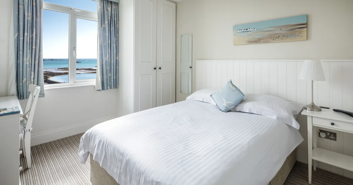 Bright seafacing single bedroom with a neatly made bed, white furniture and sea views through the window.