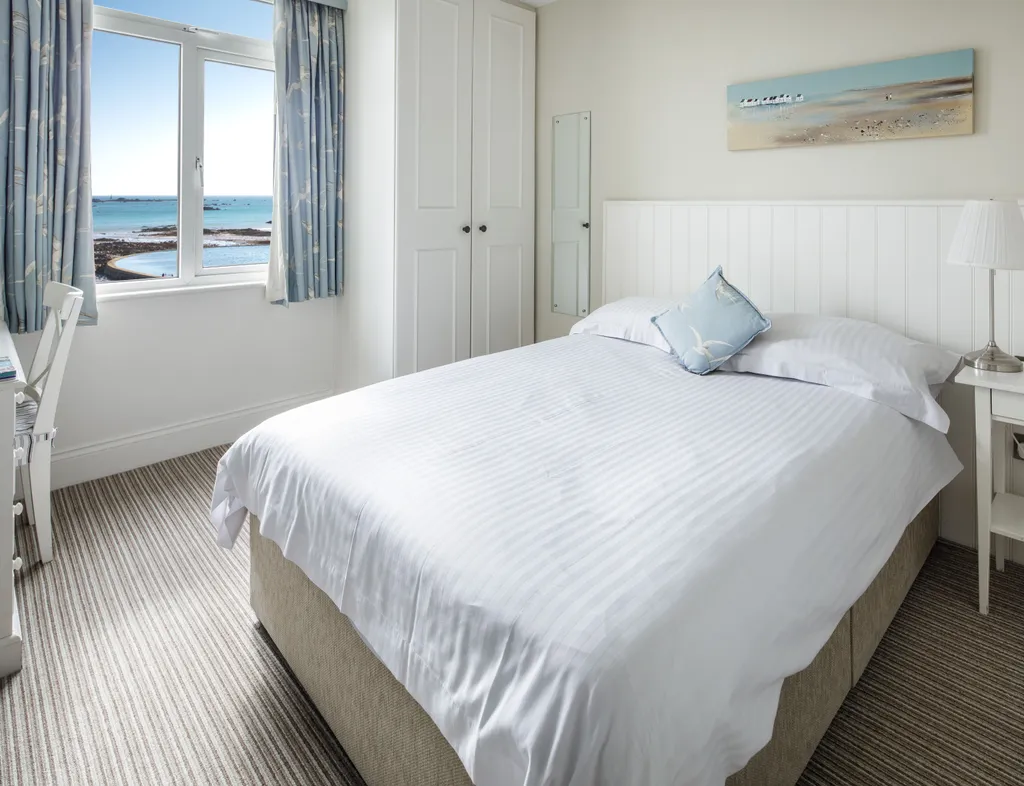 Bright seafacing single bedroom with a neatly made bed, white furniture and sea views through the window.