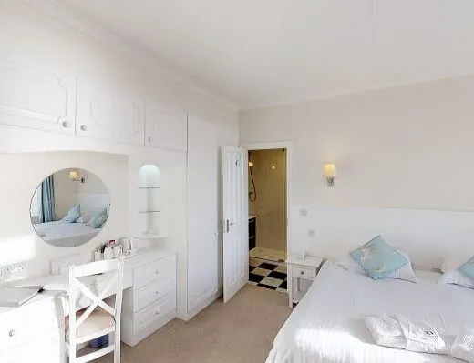 Bright classic bedroom with white furnishings, built-in wardrobe, dressing table and double bed with pale blue cushions
