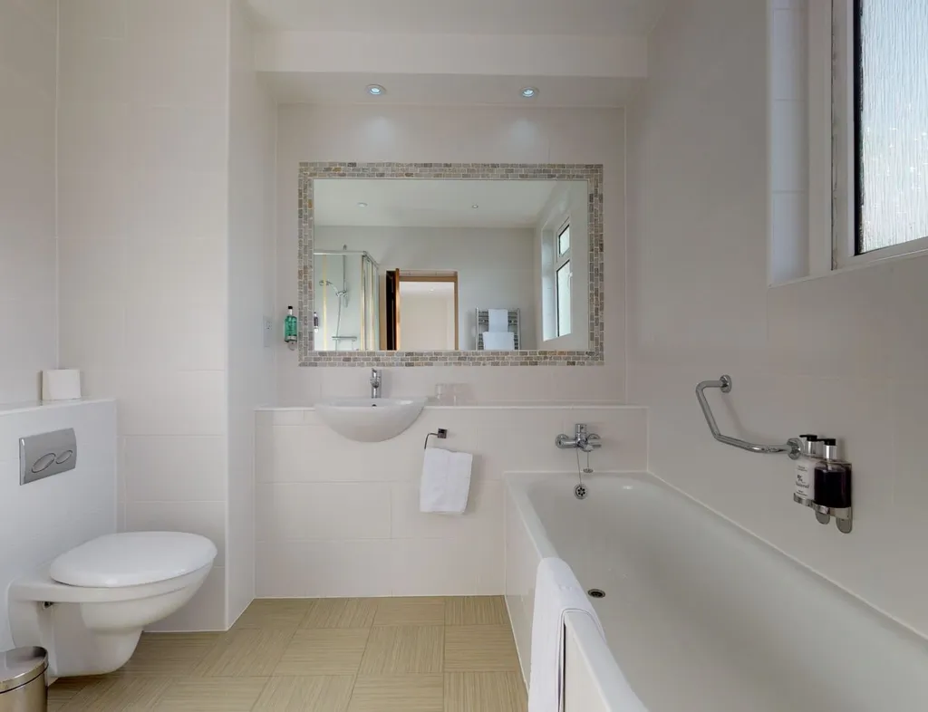 Modern white tiled bathroom with a bath, wall-mounted toilet, sink and large mirror
