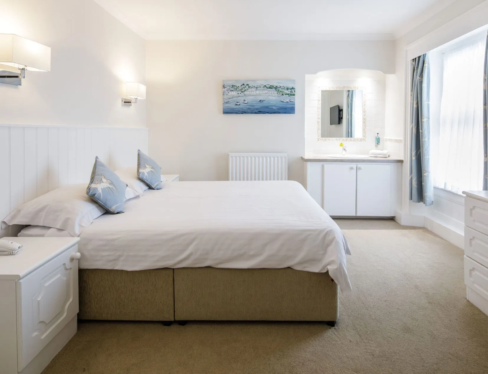 Bright double bedroom with white furnishings, blue curtains and a vanity unit