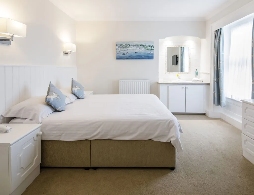 Bright double bedroom with white furnishings, blue curtains and a vanity unit