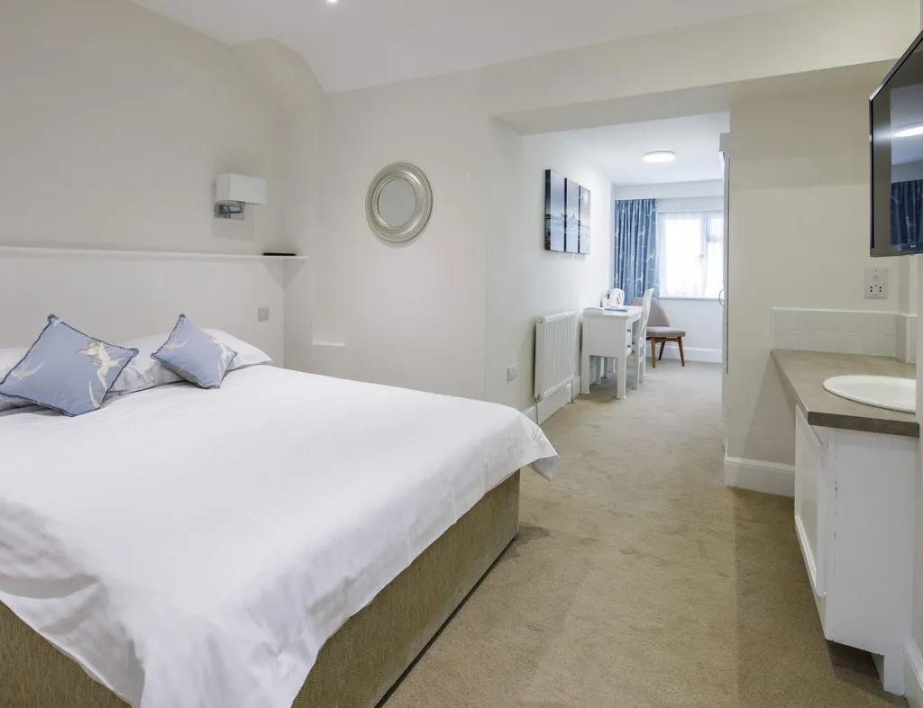 Spacious hotel bedroom with double bed, wall-mounted television, wash basin and seating area by the window