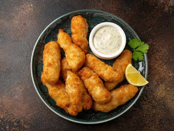Plate of golden breaded fish goujons with tartare sauce, lemon wedge and parsley