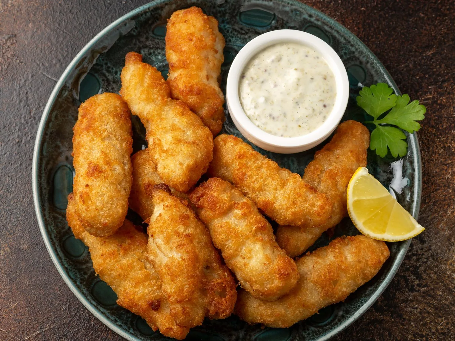 Plate of golden breaded fish goujons with tartare sauce, lemon wedge and parsley