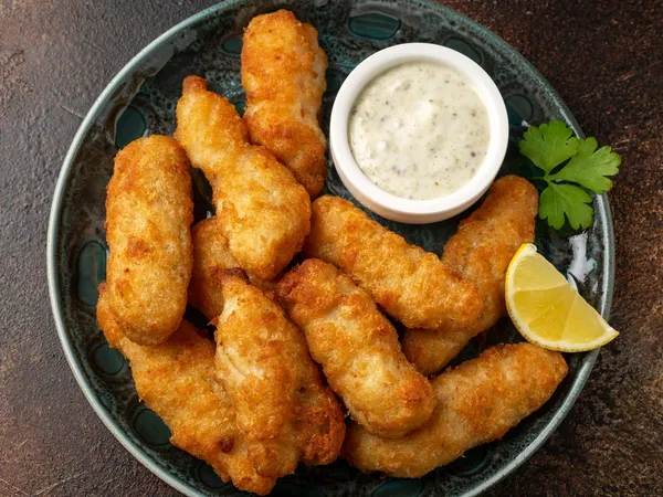 Plate of golden breaded fish goujons with tartare sauce, lemon wedge and parsley