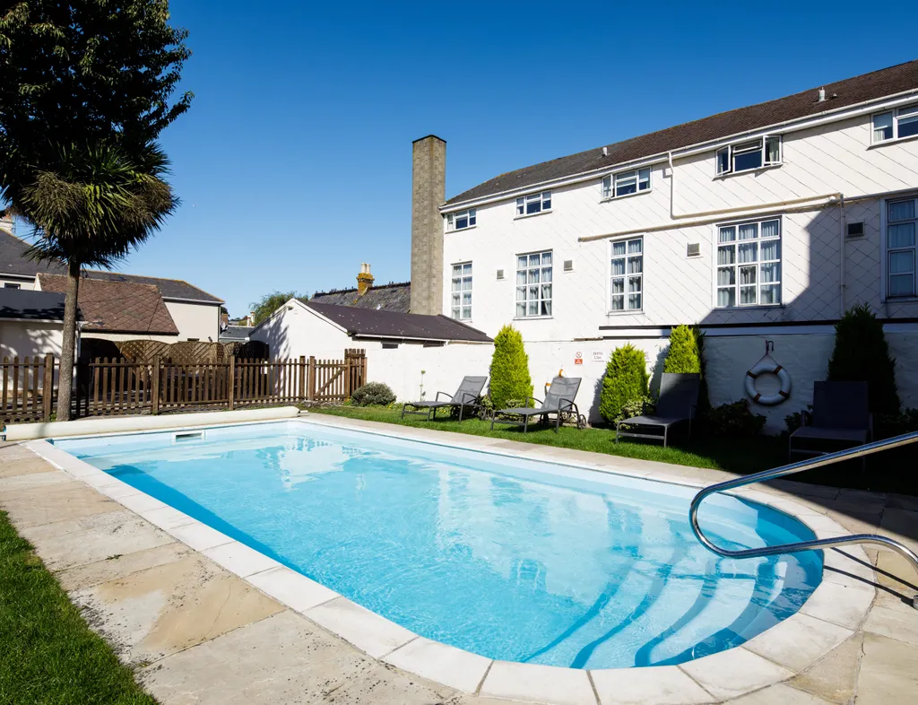 Outdoor swimming pool beside a white hotel building with sun loungers and a clear blue sky