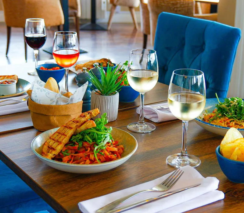 Close-up of a Coast Bistro table in the bar area set with pasta dishes, bread, crisps and glasses of red, rosé and white wine.