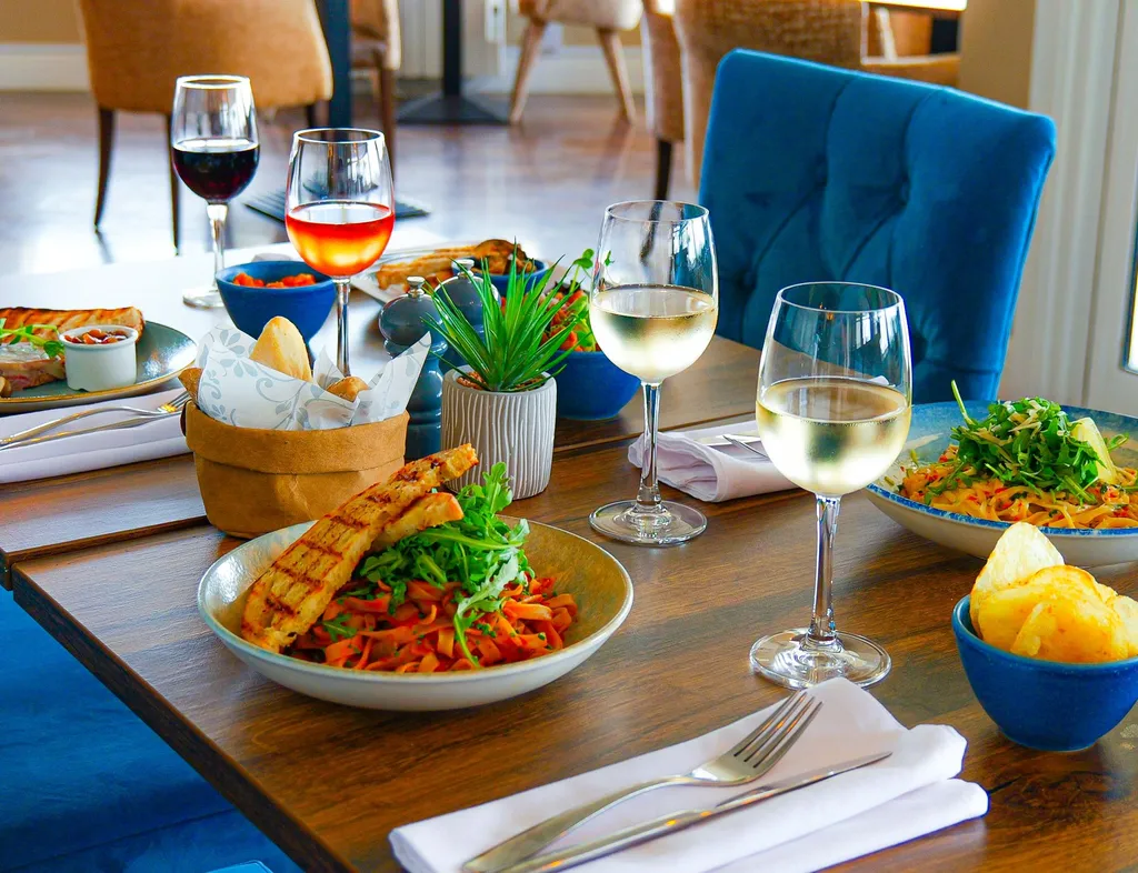 Close-up of a Coast Bistro table in the bar area set with pasta dishes, bread, crisps and glasses of red, rosé and white wine.