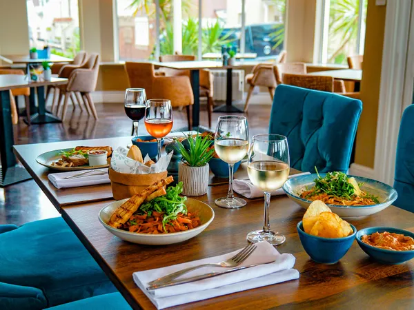 Dining table set with pasta dishes, bread, crisps and glasses of wine in the bright bar area at Coast Bistro.