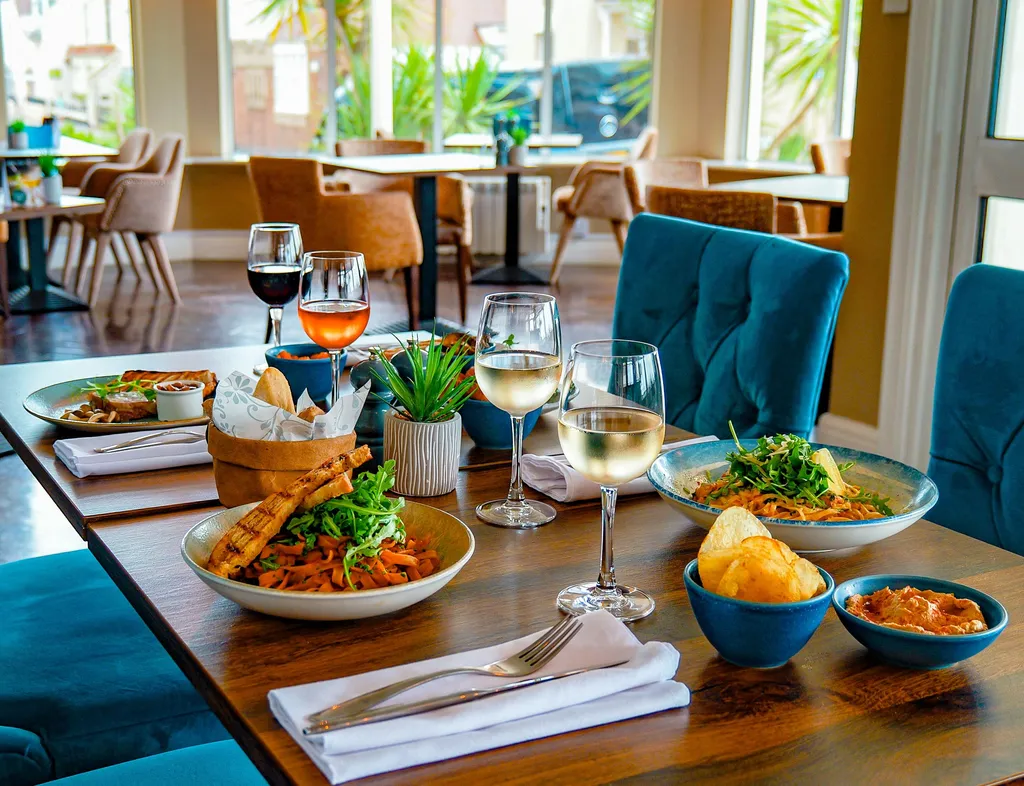 Dining table set with pasta dishes, bread, crisps and glasses of wine in the bright bar area at Coast Bistro.