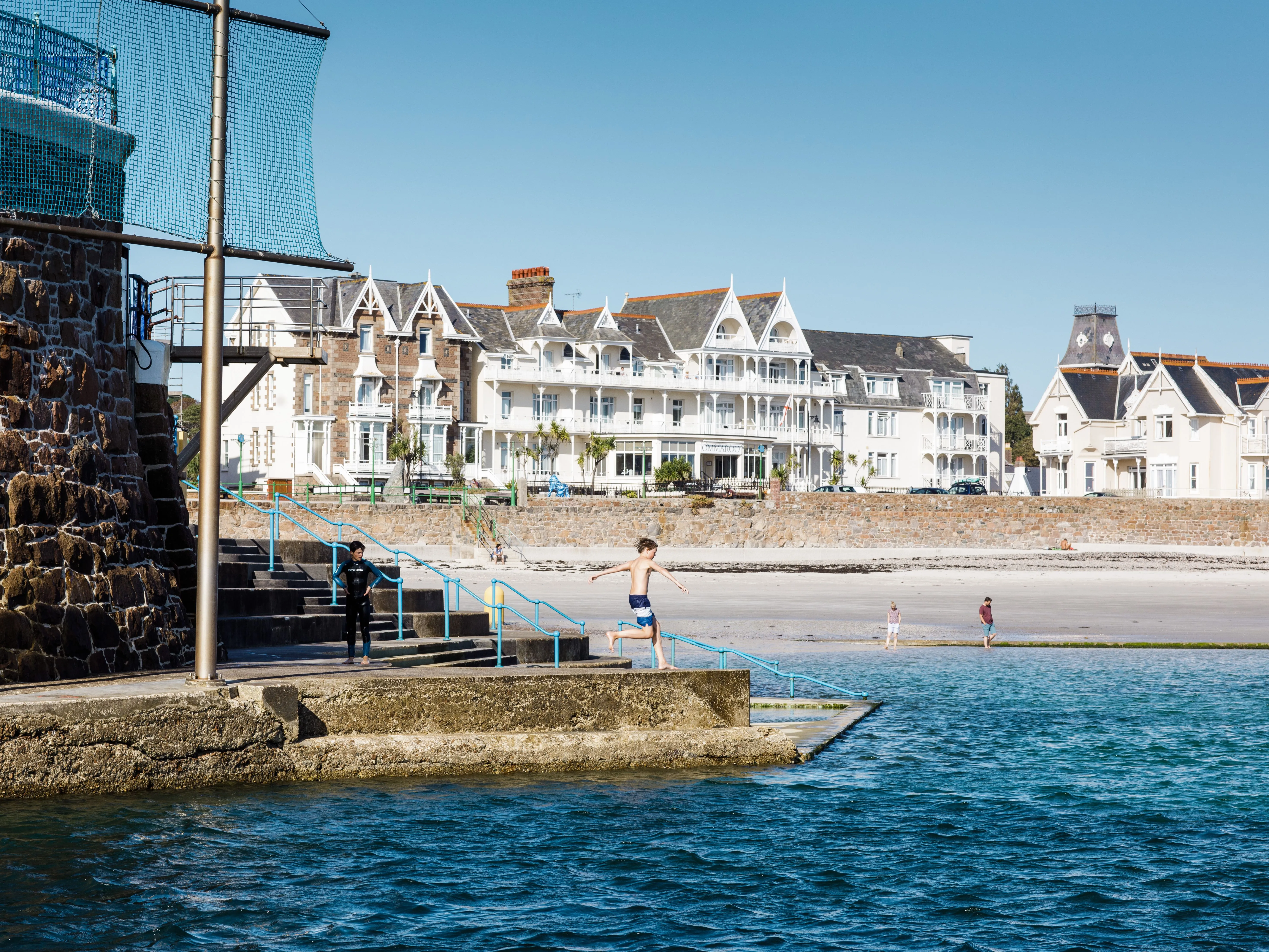 Boy jumping into the sea at Havre des Pas with beachfront buildings in the background